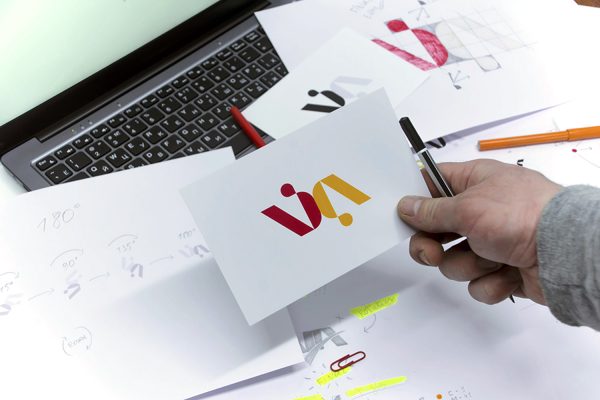 Espace de travail d'un graphiste tenant dans sa main un modèle du logo en couleur.