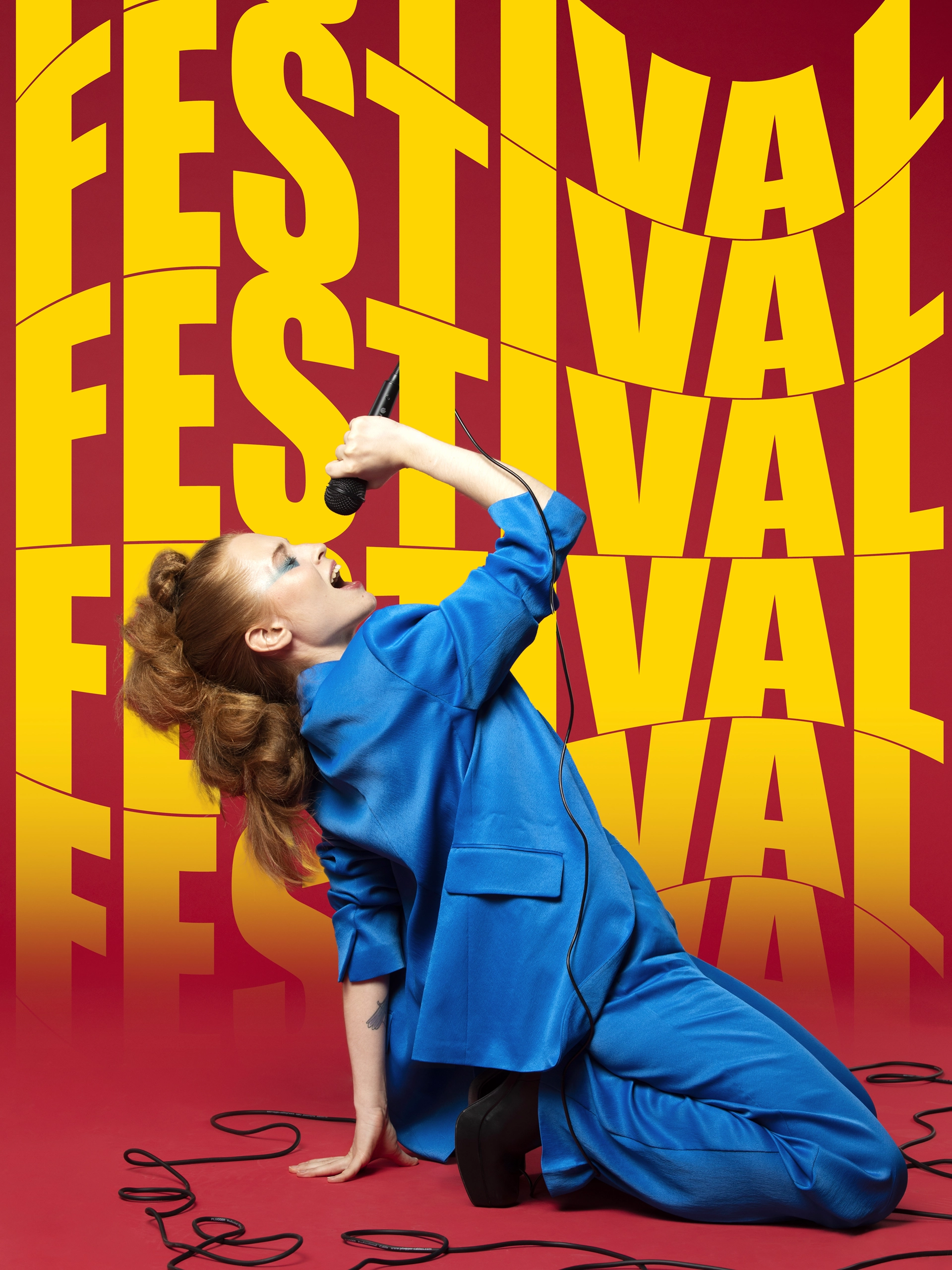Image d'une femme habillée en bleu à genou sur un sol rouge micro à la main dans le fond le mot festival ecrit plusieur fois en jaune